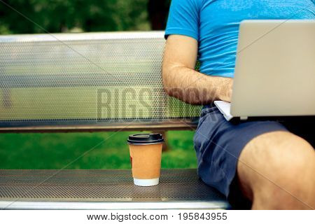 Freelance work. Casual dressed man sitting at wooden beanch inside garden working on computer.