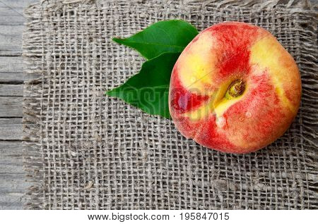 Chinese flat peach with leaves on burlap napkin.Donut peache also known as Paraguayo peach.Healthy food or Diet concept.