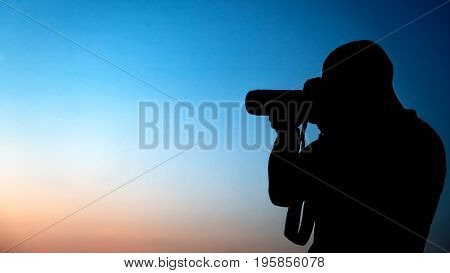 Silhouette of a photographer over blue sky background, professional photographer making picture, traveler taking photo, man at work, creative profession