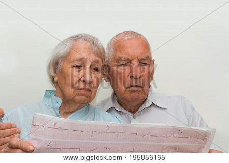 The medicine, age, health care and people concept - the sad senior woman and man looking at cardiogram on gray background
