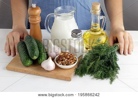 Fresh Ingredients For Cooking Tarator With Female Hands On White Wooden Table In The Kitchen.