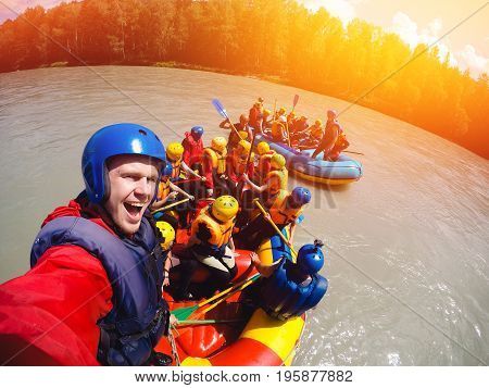 mountain Altai, RUSSIA - July 16, 2017: man in a helmet holds an action camera and makes selfie on the background of friends with oars, rafting