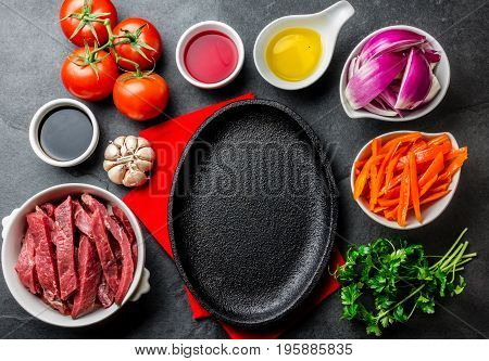 Ingredientes for cooking peruvian dish Lomo saltado - tenderloin beef, yellow chili, tomatoes, onion, oil, soy sauce, vinegar, garlik around black plate