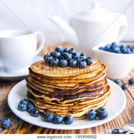 Pancakes healthy breakfast with blueberries, bog whortleberry, cup of green tea, cup of blueberries and teapot on brown wooden background