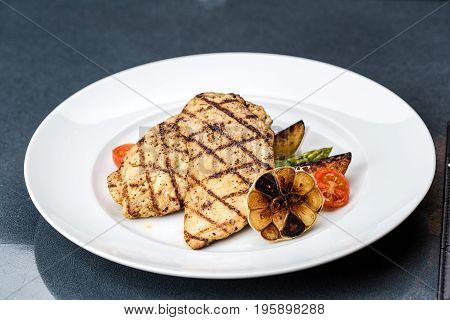Grilled chicken fillet served with french fries, asparagus and cherry tomatoes, decorated with grilled garlic and baby spinach