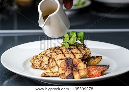 Grilled chicken fillet served with french fries, asparagus and cherry tomatoes, decorated with grilled garlic and baby spinach