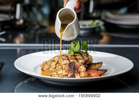 Grilled chicken fillet served with french fries, asparagus and cherry tomatoes, decorated with grilled garlic and baby spinach