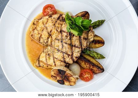 Grilled chicken fillet served with french fries, asparagus and cherry tomatoes, decorated with grilled garlic and baby spinach