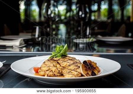 Grilled chicken fillet served with french fries, asparagus and cherry tomatoes, decorated with grilled garlic and baby spinach