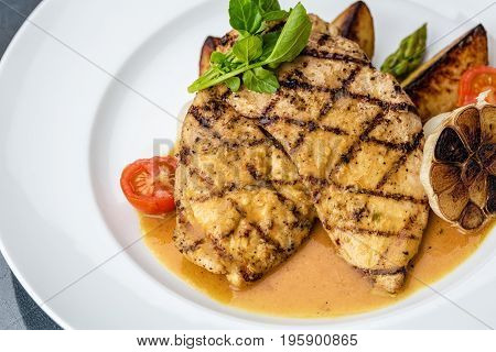 Grilled chicken fillet served with french fries, asparagus and cherry tomatoes, decorated with grilled garlic and baby spinach