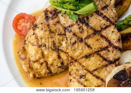 Grilled chicken fillet served with french fries, asparagus and cherry tomatoes, decorated with grilled garlic and baby spinach