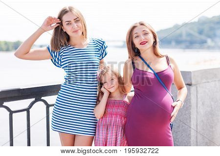Samesex lesbian family with child on a walk in the park near the river. Lesbians mothers with adopted child, happy family, pregnant couple with kid