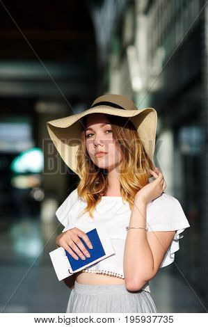 Pretty girl in a wide-brimmed hat with the passport and tickets in a hand. Girl posing. Railway station. Summer holiday.