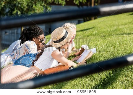 mutiethnic students lying on green grass while studying in park