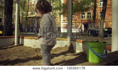 A kid playing in sandbox on a playground in a courtyard