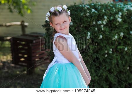 Cute small girl dressed in blue and white dress with a wreath of artificial flowers on her head child in a festive dress on a nature background look at the camera