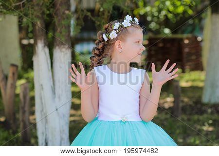 girl with arms raised looks aside child with a wreath of artificial flowers on her head