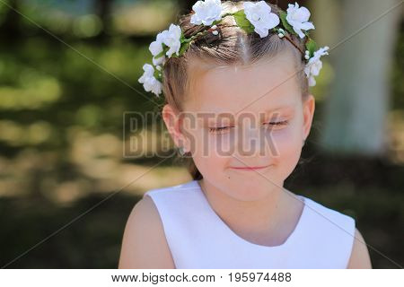 little girl is shy and looks down a child with a wreath of artificial flowers on her head