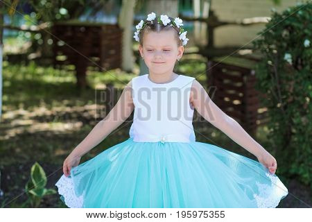Cute Small  Girl Wearing A White And Blue Dress Posing Over Nature Background, Child With A Wreath O