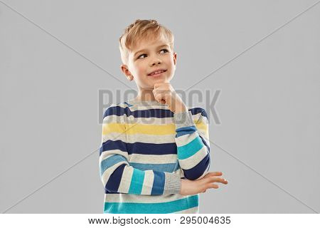 childhood, expressions and people concept - portrait of smiling little boy in striped pullover thinking over grey background