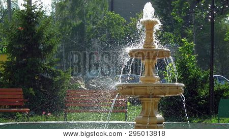 On A Sunny Summer Day. Vintage Fountain On A Background Of Green Trees.