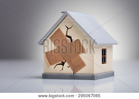 Broken House Model With Crossed Band Aid On Desk