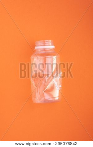 Squashed plastic bottle on orange background. Plastic utilisation concept. Ecological problem, global environment.