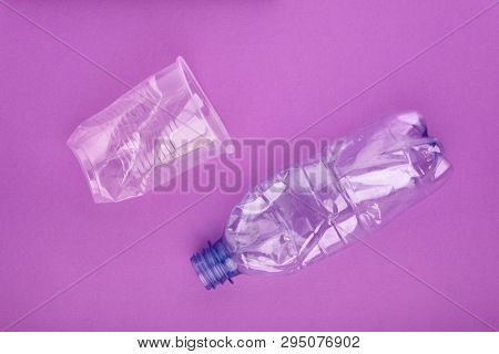 Squashed plastic bottle and cup on purple background. Plastic utilisation concept. Ecological problem, global environment.