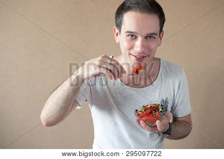 Slim Handsome Boy Eating Salad Over Wooden Background. Studio Shot