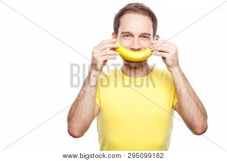 Young Man Holding Banana Near Face Like A Smile. Studio Shot