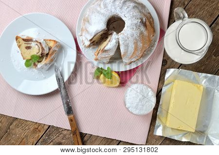Top View Of Sliced Of Bundt Cake Sprinkled With Sugar, Lemon, Melissa, Milk, Eggs And Butter