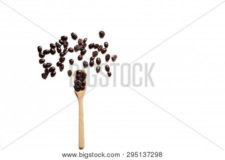 In Selective Focus Many Dark Roasted Coffee Beans On A Wood Spoon And On A Floor, White Isolated Bac