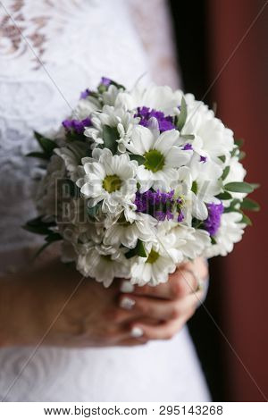 A Small Wedding Bouquet Of White Chrysanthemums And Purple Flowers Statice In The Hands Of The Bride