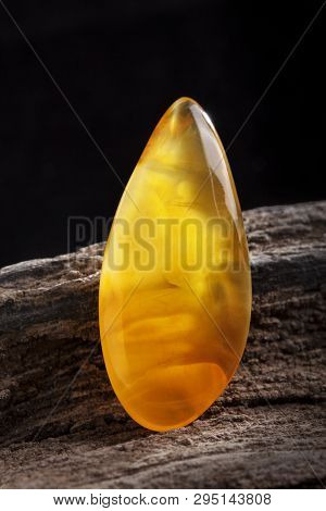 Natural Amber. A Piece Of Yellow Opaque Natural Amber On Large Piece Of Dark Stoned Wood.