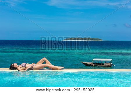 one caucasian woman enjoying vacations  sunbathing on a infinity swimming pool by the seaside looking at the idian ocean Muyuni  in Unguja aka Zanzibar Island Tanzania East Africa