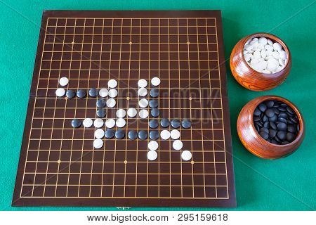 Top View Of Gameplay Of Go Game And Playing Stones In Bowls And Wooden Board On Green Table
