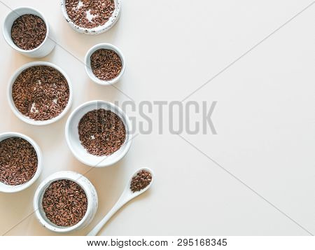 Flax Seeds On White Or Light Beige Background. Set Of Small Bowls With Organic Flax Seed Or Linen Se