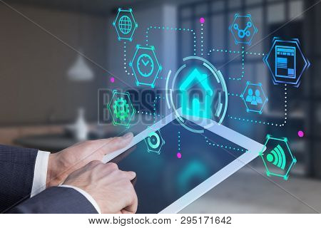 Hand Of Man Using Tablet With Glowing Smart Home Interface Over Blurred Room Background. Concept Of 
