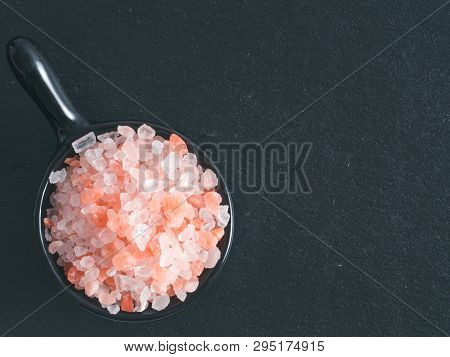 Himalayan Pink Salt In Small Black Bowl On Black Stone Background. Copy Space
