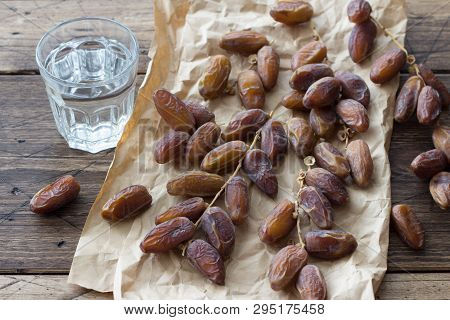 Dried Dates Fruits On A Branch And A Glass Of Water On A Wooden Table. Traditional Fast Breaking, Mu
