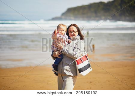 Grandmother And Granddaughter Enjoying Atlantic Ocean On The Beach. Middle Aged Woman Holding Little