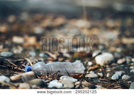 Environmental Pollution Plastic Bottle With Blue Lid Brown Liquid Inside On The Beach Among Stones A