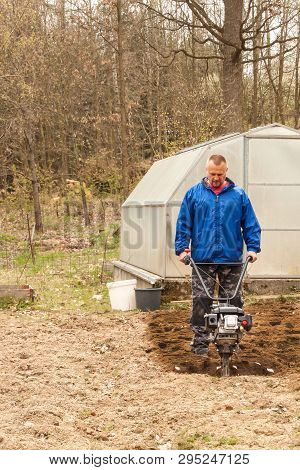 Spring Preparation Soil For Seeding With Tiller. Spring Work In The Garden. Farmer Plows The Land Wi
