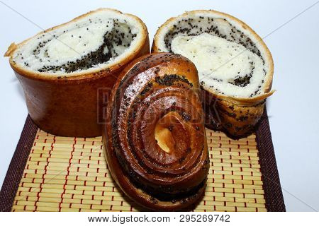 Three Pieces Of Roll With Poppy Seed Filling Lie On A Napkin, Placed On A White Background