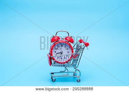 Red Retro Alarm Clock In Shopping Cart On Blue Background. Shopping Time, Market, Consumer Concept.