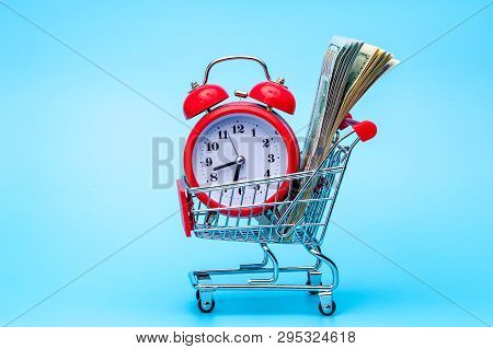Red Retro Alarm Clock And Dollar Bills In Shopping Cart On Blue Background. Shopping Time, Market, C