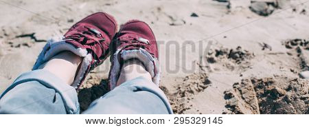 Feet Of Young Woman In Sport Footwear And Jeans Relaxing After Hiking On Sand Beach. Pov. Adventure 