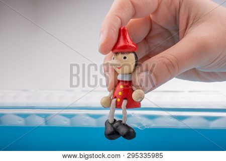 Hand Holding Wodden Puppet Pinocchio On In Blue Water