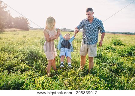 Mother And Father Swinging Son In Sunnny Summer Day