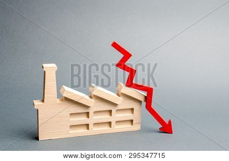 Factory Figurine And Red Down Arrow. The Concept Of A Fall In The Level Of Production And The Level 